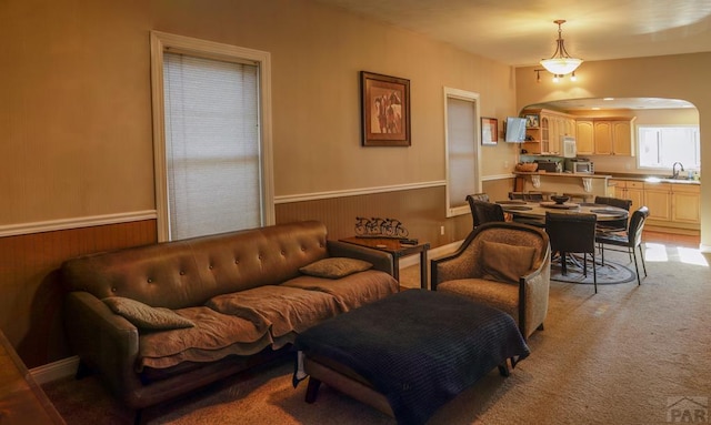 709 Cimarron Ave, La Junta, CO 81050 - living area featuring wainscoting, arched walkways, light colored carpet, and wooden walls