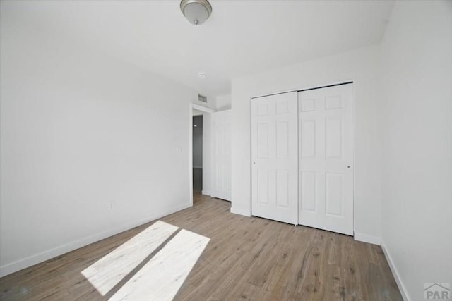 unfurnished bedroom featuring baseboards, visible vents, wood finished floors, and a closet