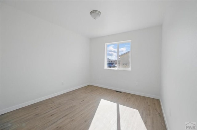 empty room featuring baseboards, wood finished floors, and visible vents