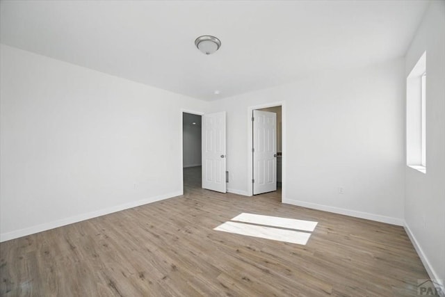 unfurnished bedroom with a walk in closet, baseboards, and wood finished floors