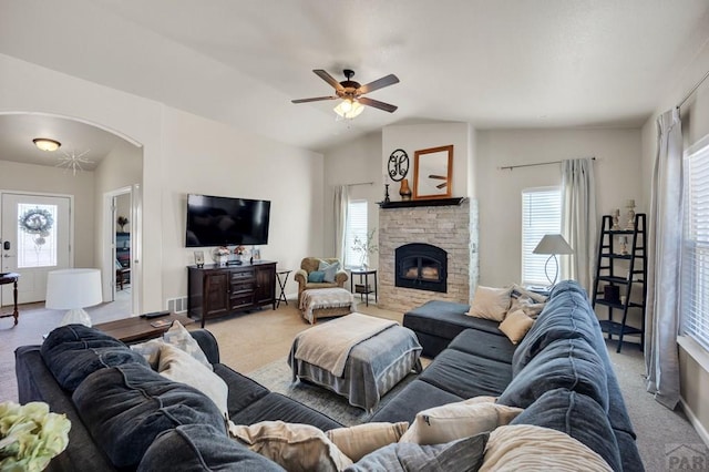 living room with a ceiling fan, a stone fireplace, arched walkways, light colored carpet, and lofted ceiling