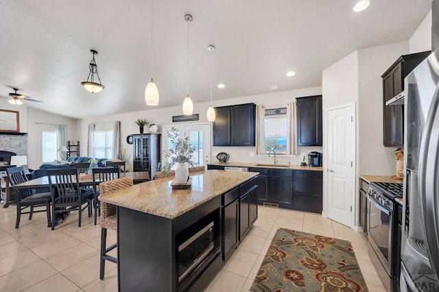 kitchen with light tile patterned floors, a sink, light stone countertops, a kitchen island, and appliances with stainless steel finishes