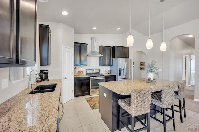 kitchen with a sink, arched walkways, wall chimney range hood, light stone countertops, and appliances with stainless steel finishes