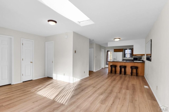 living area featuring a skylight, light wood-style flooring, and baseboards