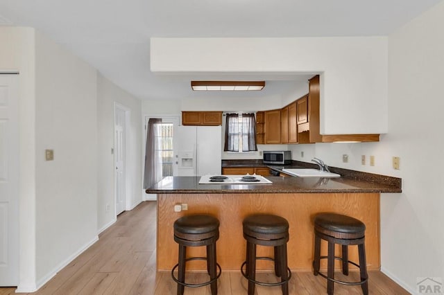 kitchen featuring dark countertops, a sink, white appliances, a peninsula, and a kitchen breakfast bar