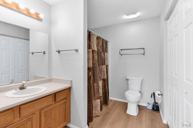 bathroom with curtained shower, toilet, wood finished floors, vanity, and a closet