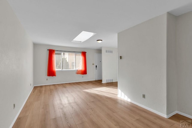 empty room featuring light wood-style floors, a skylight, visible vents, and baseboards