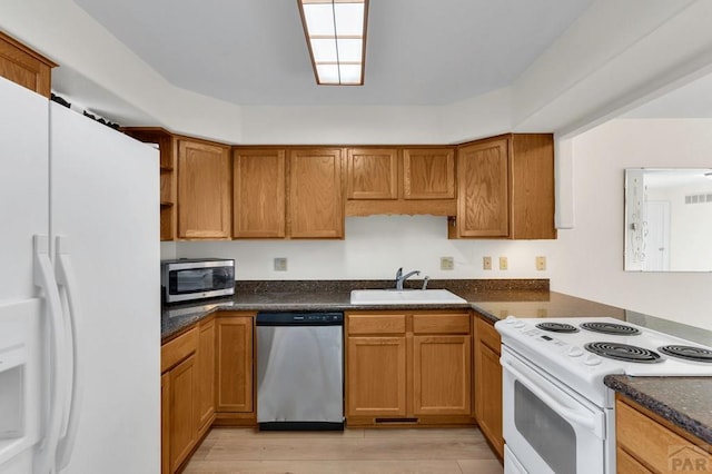 kitchen featuring brown cabinetry, dark stone countertops, stainless steel appliances, open shelves, and a sink