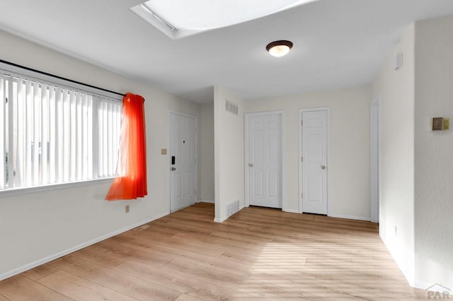 unfurnished bedroom featuring baseboards, light wood-style flooring, visible vents, and two closets