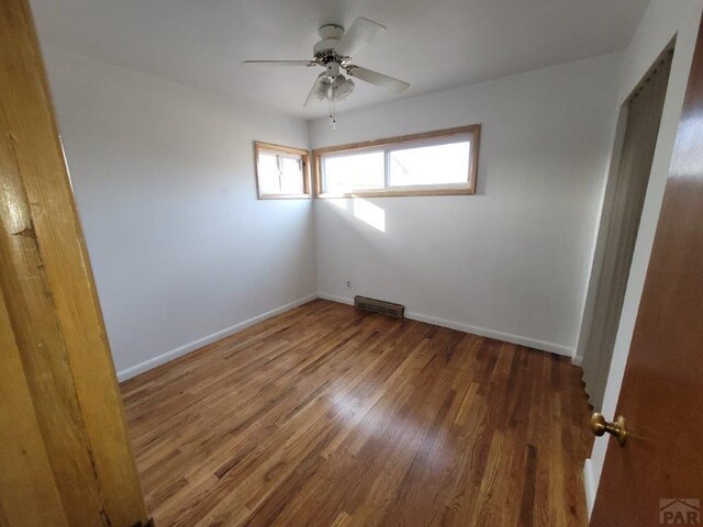 empty room featuring a ceiling fan, wood finished floors, visible vents, and baseboards