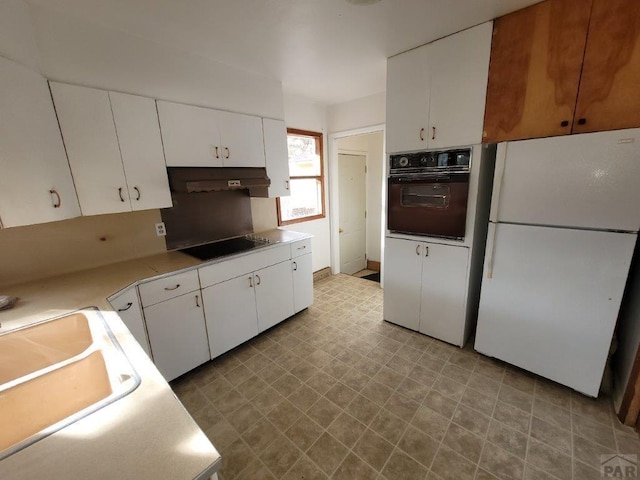 kitchen with oven, freestanding refrigerator, black electric cooktop, light countertops, and white cabinetry