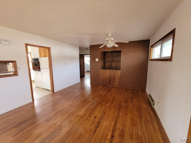 spare room with a ceiling fan, baseboard heating, built in shelves, and wood finished floors