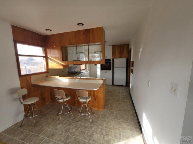 kitchen featuring a peninsula, brown cabinetry, light countertops, and freestanding refrigerator