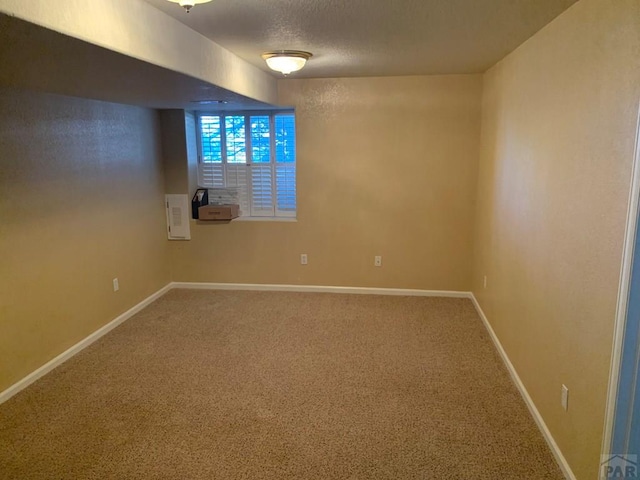 carpeted spare room featuring a textured ceiling and baseboards