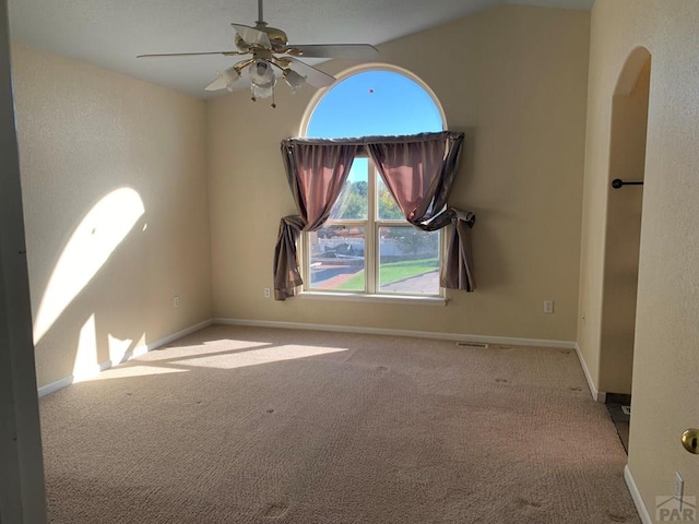 empty room with ceiling fan, arched walkways, light colored carpet, baseboards, and vaulted ceiling