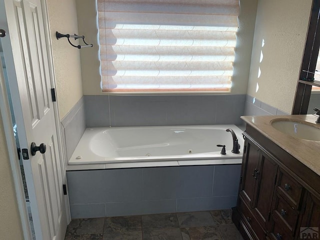 bathroom featuring a textured wall, a tub with jets, and vanity