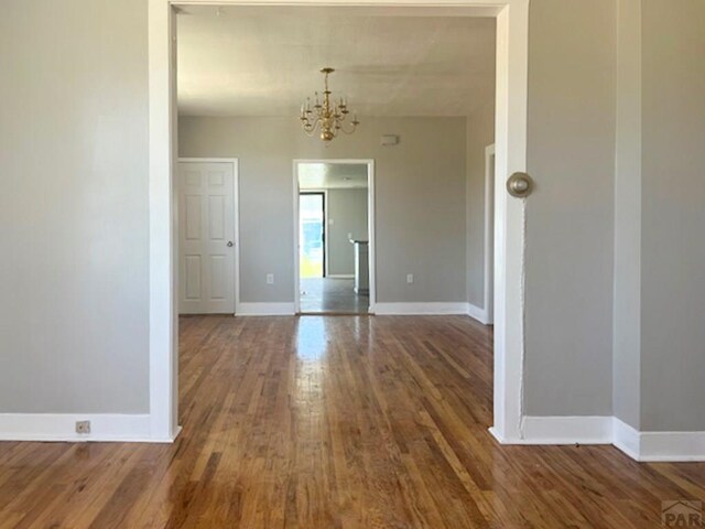 unfurnished dining area with dark wood-type flooring, baseboards, and an inviting chandelier