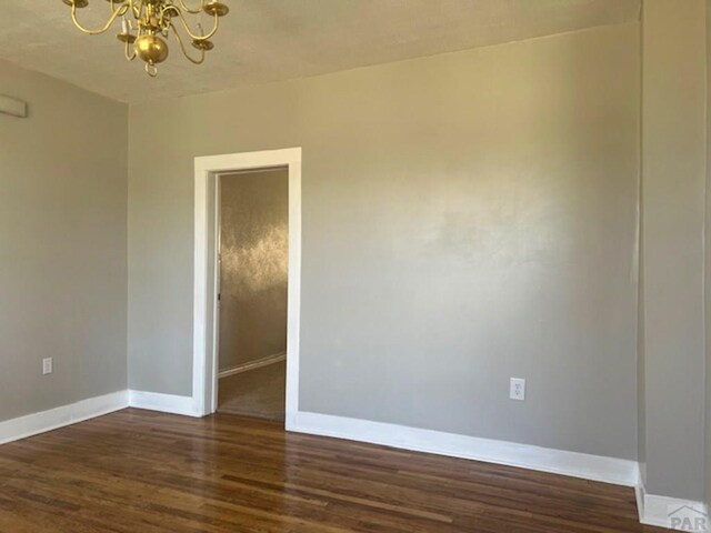 unfurnished room featuring dark wood-type flooring, baseboards, and an inviting chandelier