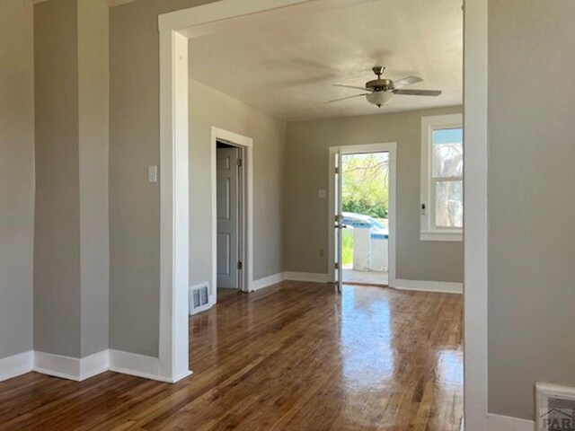 interior space with a ceiling fan, visible vents, dark wood finished floors, and baseboards