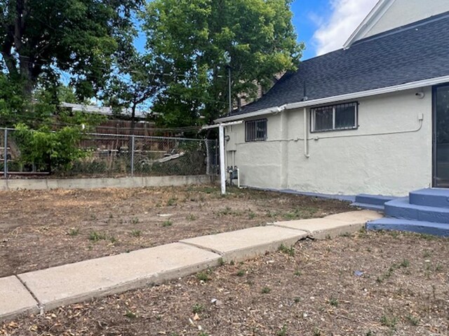 view of side of home featuring entry steps, roof with shingles, fence, and stucco siding