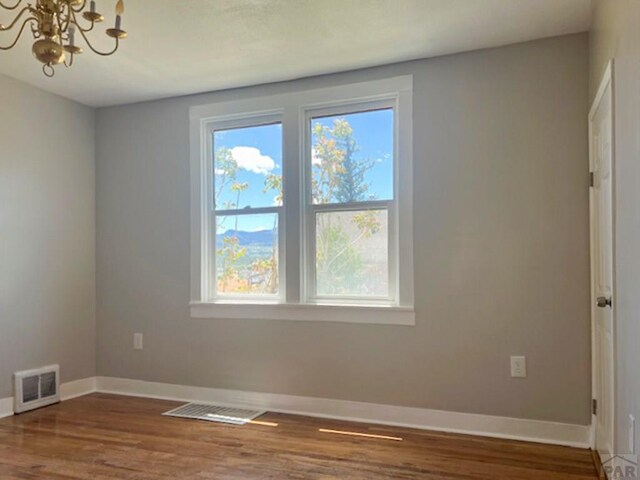 unfurnished room with an inviting chandelier, baseboards, visible vents, and wood finished floors