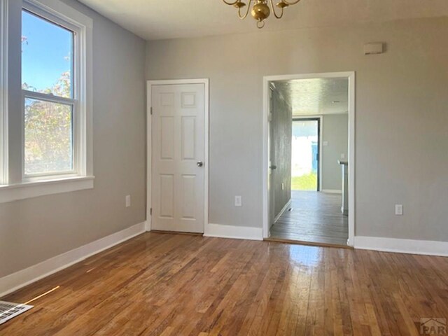 spare room featuring an inviting chandelier, visible vents, baseboards, and wood finished floors