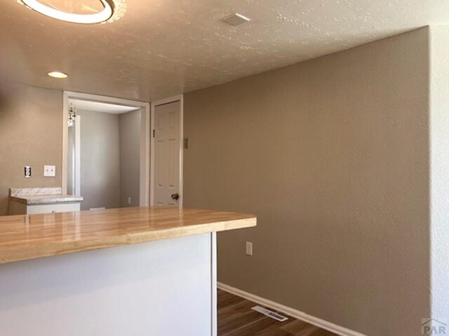 kitchen featuring a textured ceiling, dark wood-style flooring, visible vents, baseboards, and light countertops