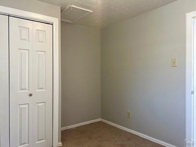 spare room featuring carpet floors, attic access, and baseboards