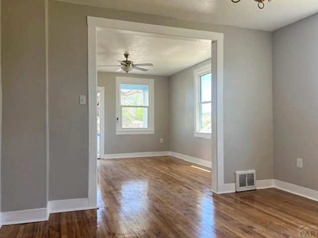 unfurnished room with ceiling fan with notable chandelier, wood finished floors, visible vents, and baseboards