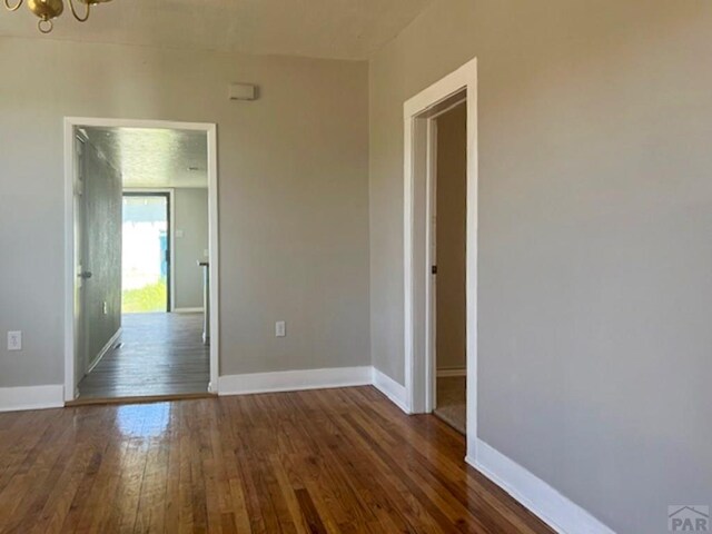 empty room featuring an inviting chandelier, baseboards, and dark wood-style flooring