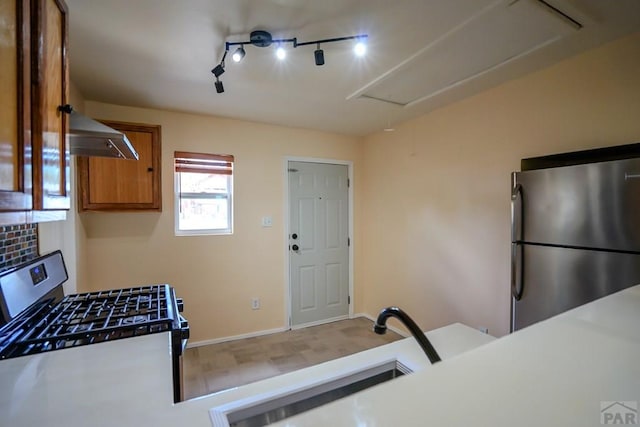 202 Pinon St, Walsenburg, CO 81089 - kitchen with appliances with stainless steel finishes, brown cabinetry, track lighting, wall chimney range hood, and light countertops