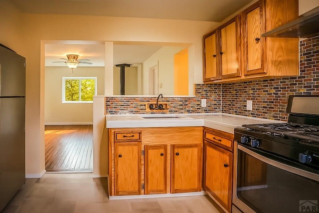 202 Pinon St, Walsenburg, CO 81089 - kitchen featuring black range with gas cooktop, freestanding refrigerator, wall chimney exhaust hood, and brown cabinets