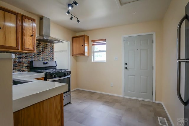 202 Pinon St, Walsenburg, CO 81089 - kitchen featuring gas range, wall chimney exhaust hood, brown cabinetry, light floors, and tasteful backsplash