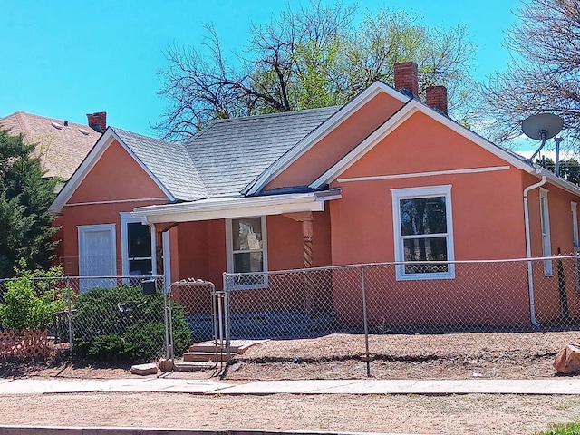 view of front facade featuring a fenced front yard, a chimney, a gate, and stucco siding