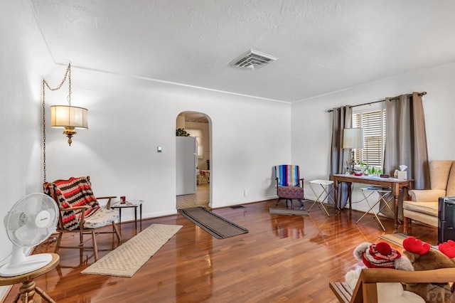 living area featuring arched walkways, wood finished floors, visible vents, and baseboards