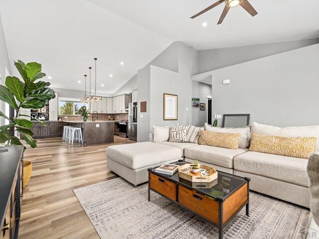 living room with light wood-style flooring, high vaulted ceiling, ceiling fan, and recessed lighting