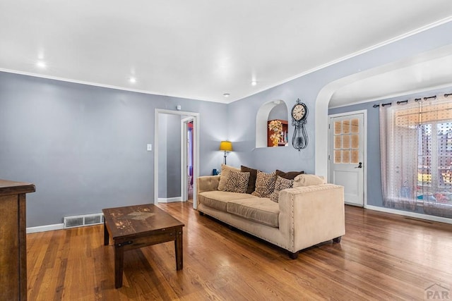 living area featuring visible vents, crown molding, baseboards, and wood finished floors