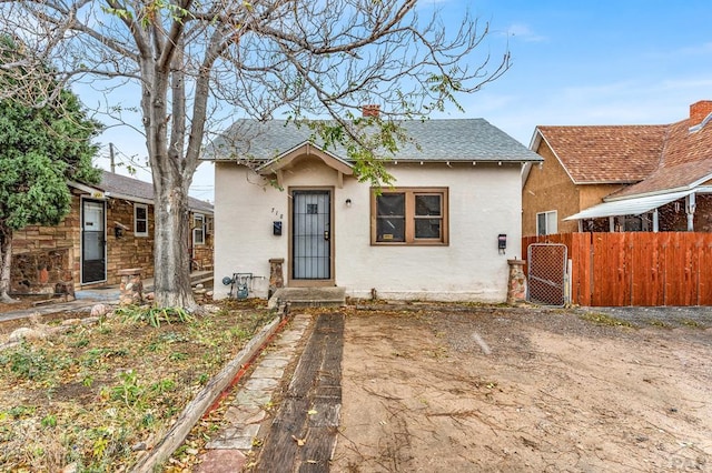 bungalow featuring a shingled roof, fence, a chimney, and stucco siding