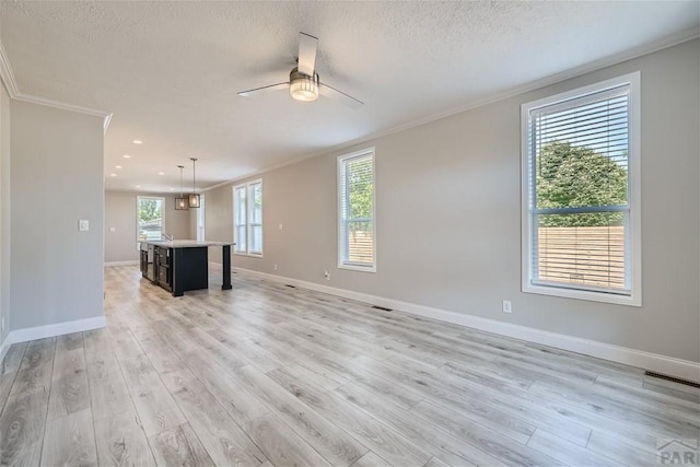 unfurnished living room with a healthy amount of sunlight, crown molding, light wood-style flooring, and a textured ceiling