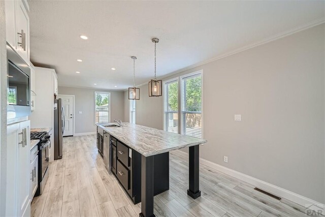 kitchen featuring a kitchen island with sink, white cabinets, dark cabinetry, appliances with stainless steel finishes, and pendant lighting