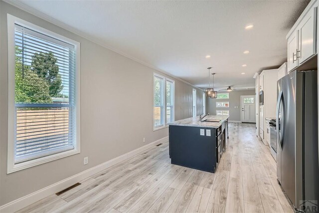 kitchen with decorative light fixtures, a center island with sink, visible vents, appliances with stainless steel finishes, and white cabinets