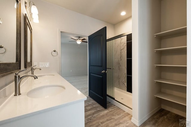 bathroom featuring double vanity, wood finished floors, a stall shower, and a sink