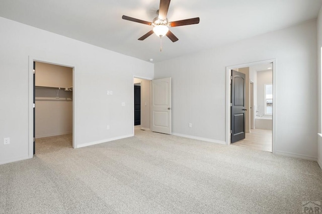 unfurnished bedroom featuring light carpet, baseboards, ensuite bath, a spacious closet, and a closet