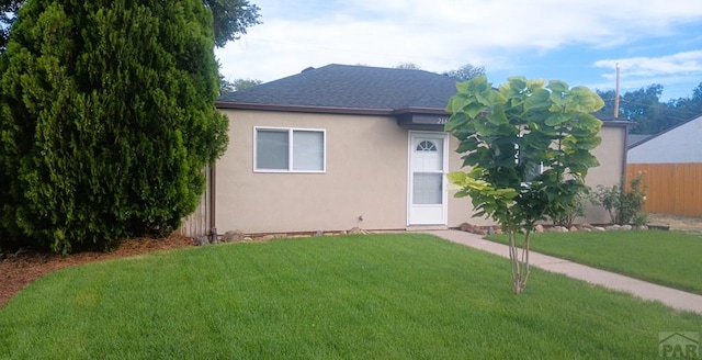 view of front of house featuring a front yard, roof with shingles, fence, and stucco siding