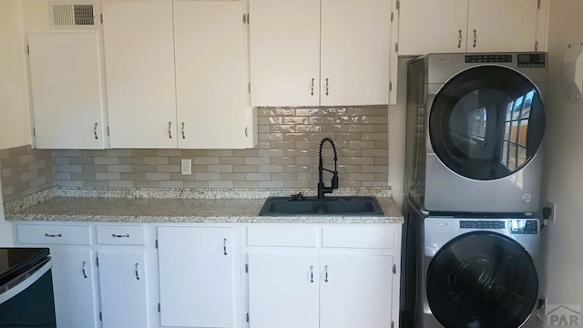 washroom with laundry area, visible vents, a sink, and stacked washer / drying machine