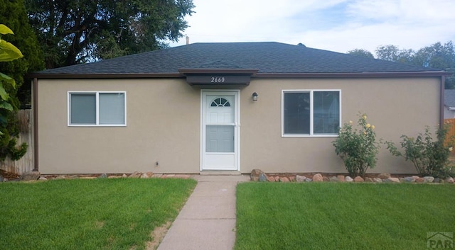 view of front of home with roof with shingles, a front yard, and stucco siding