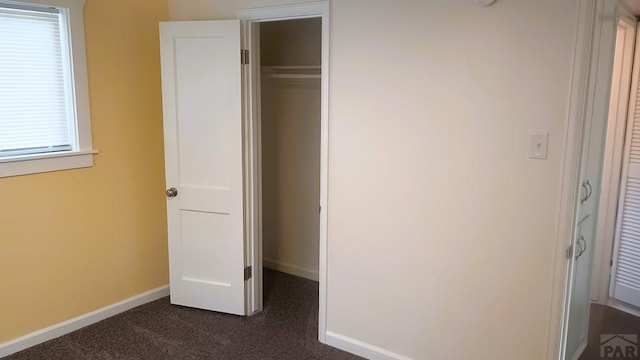 unfurnished bedroom featuring dark colored carpet, a closet, and baseboards