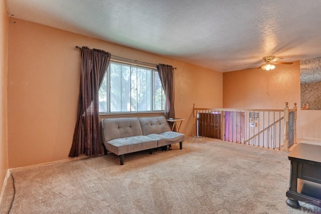 living area featuring carpet, a ceiling fan, a textured ceiling, and an upstairs landing