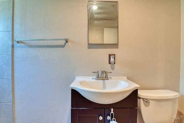 bathroom featuring toilet, a textured wall, and vanity