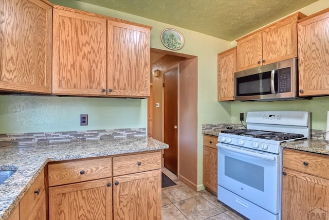 kitchen featuring light stone countertops, white gas range oven, stainless steel microwave, and a textured ceiling